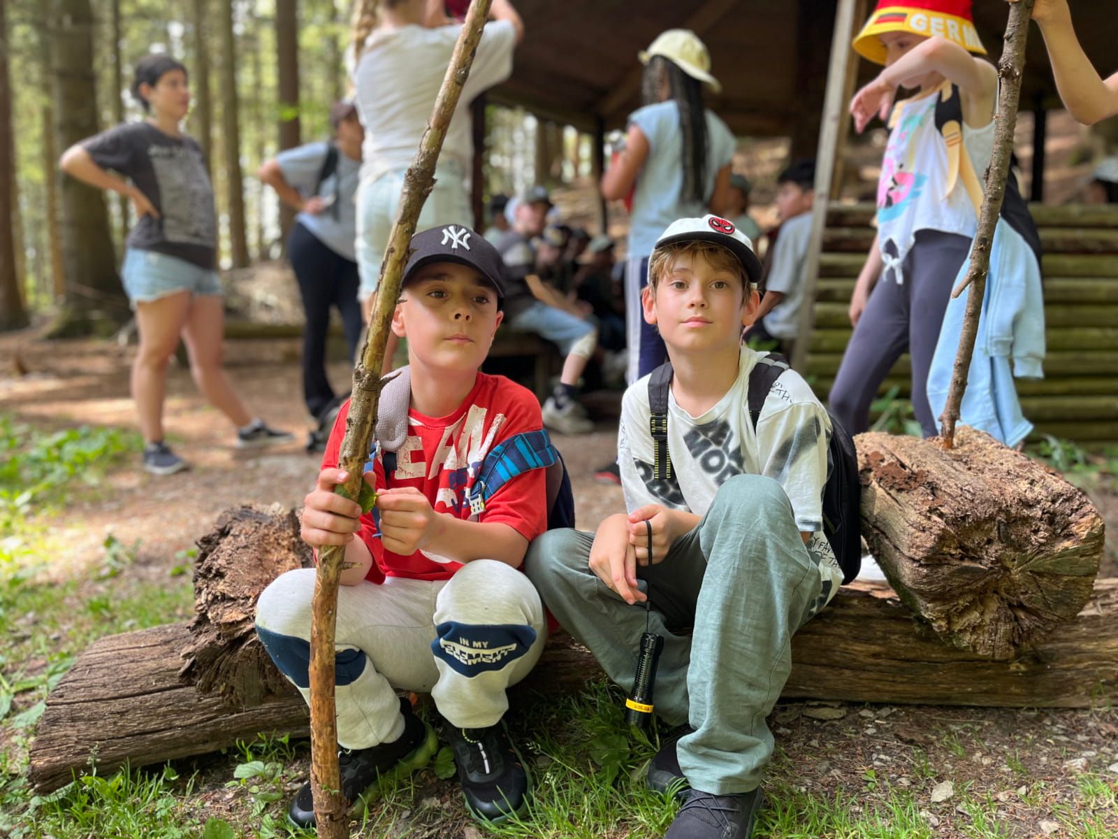 Zwei Kinder sitzen im Vordergrund vor einer Wanderhütte