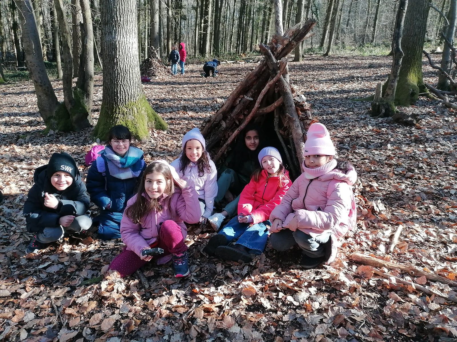 Sieben Kinder sitzen vor einem selbstgebauten Unterschlupf im Wald