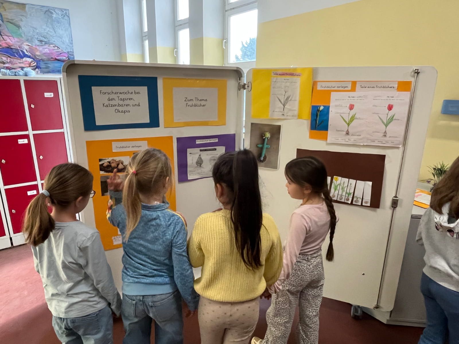 vier Kinder betrachten Plakate zum Thema Frühblüher
