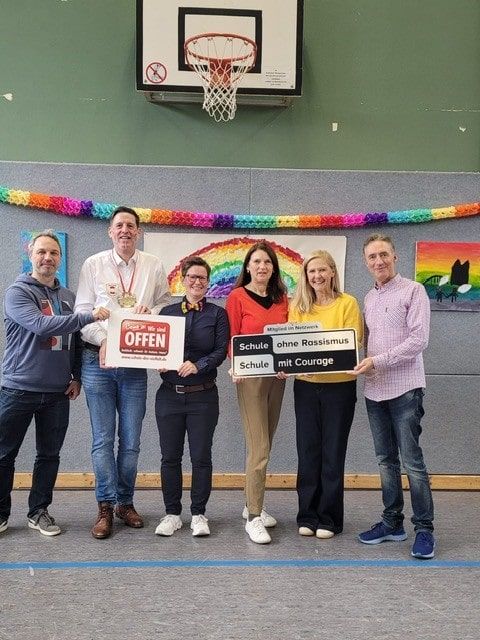 Menschen halten die Siegel der Netzwerke „Schule ohne Rassismus – Schule mit Courage“ und „Schule der Vielfalt“ hoch