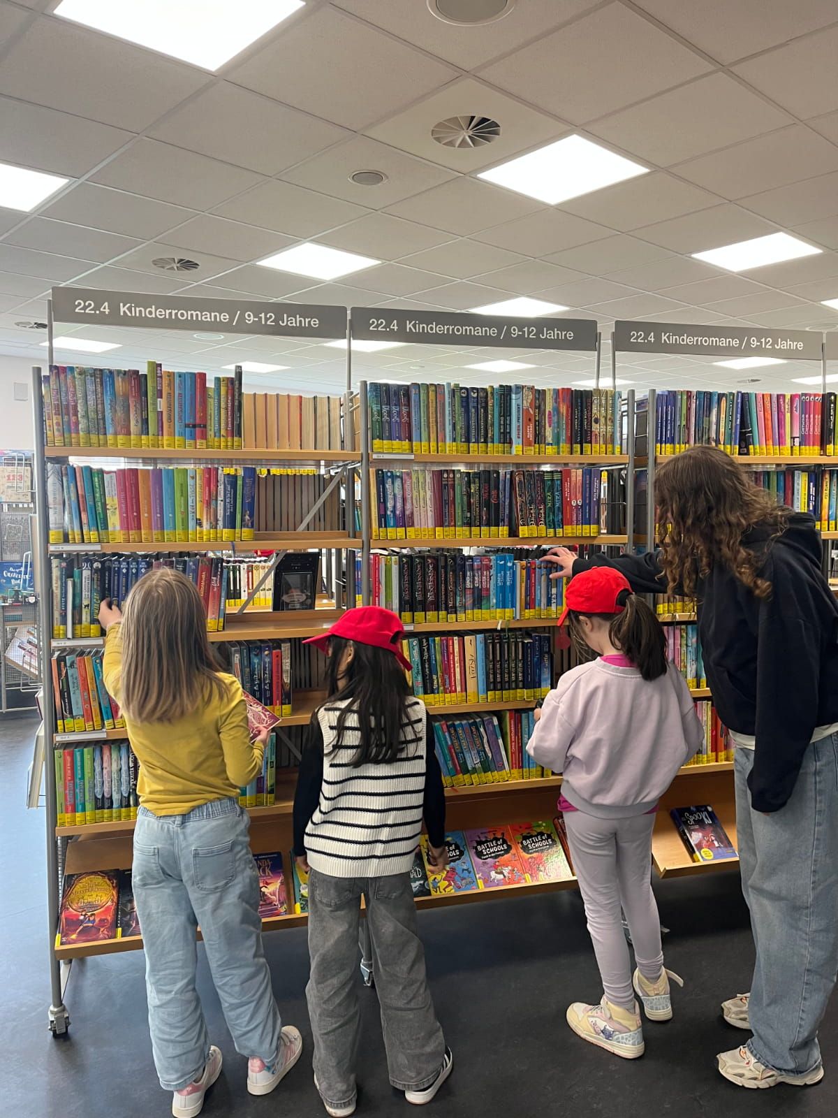 vier Kinder sehen ich Bücher in einem Bibliotheksregal an