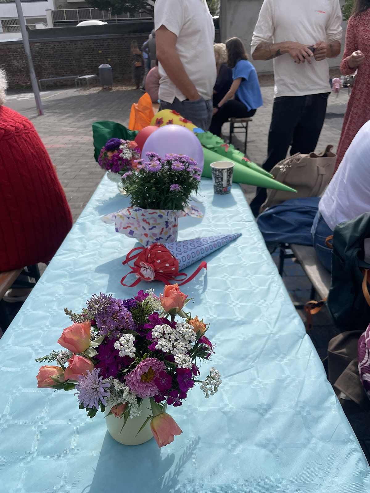 Blumen und kleine Zuckertüten liegen auf einem schmalen Tisch auf dem Schulhof