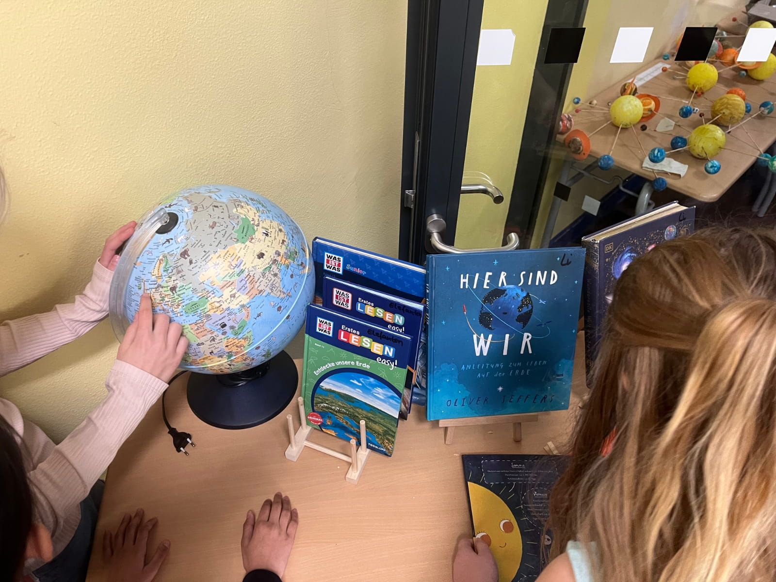 Kinder betrachten einen Globus und ausgewählte Bücher dazu