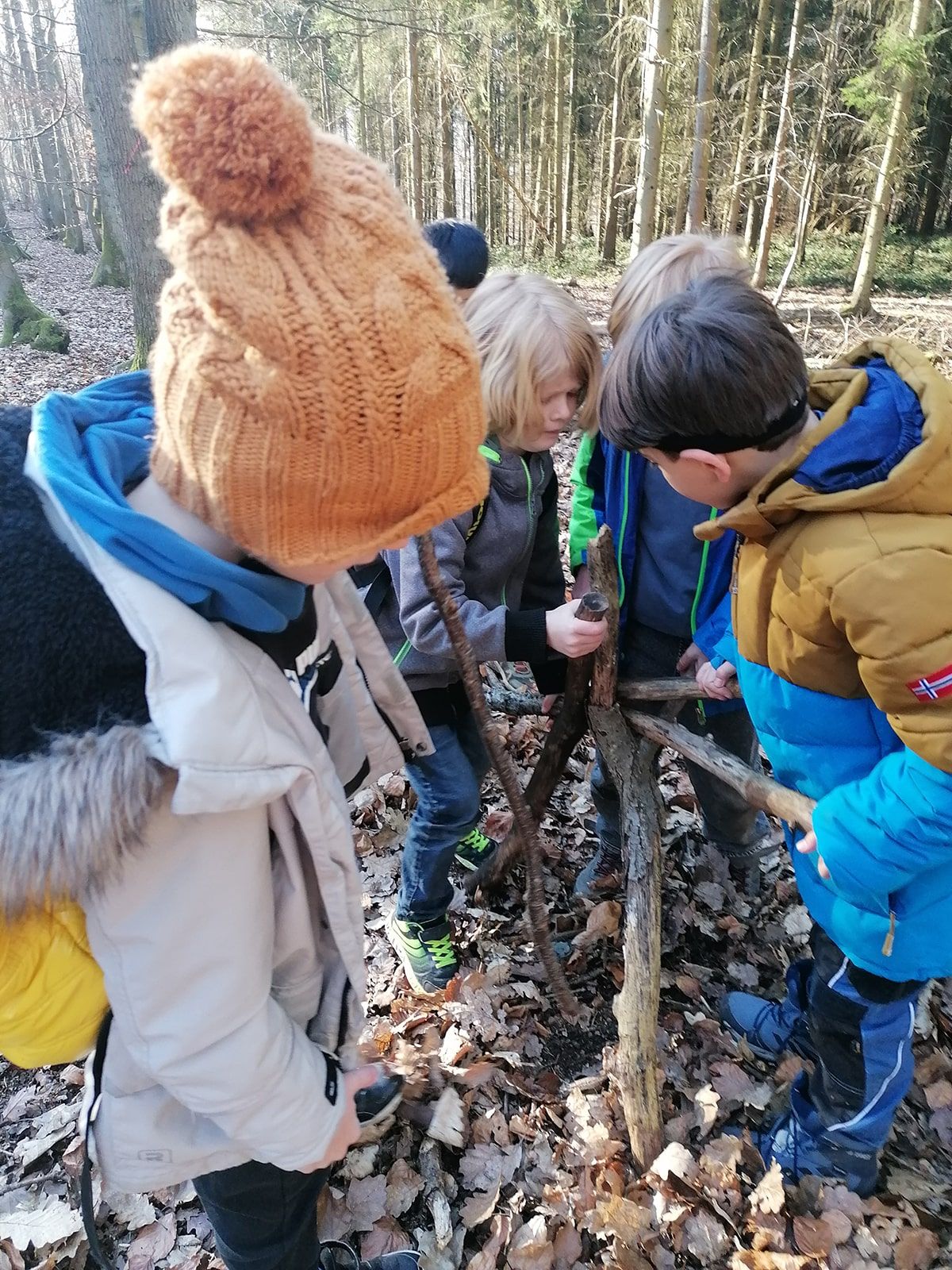 Vier Kinder bauen mit Holzästen im Wald
