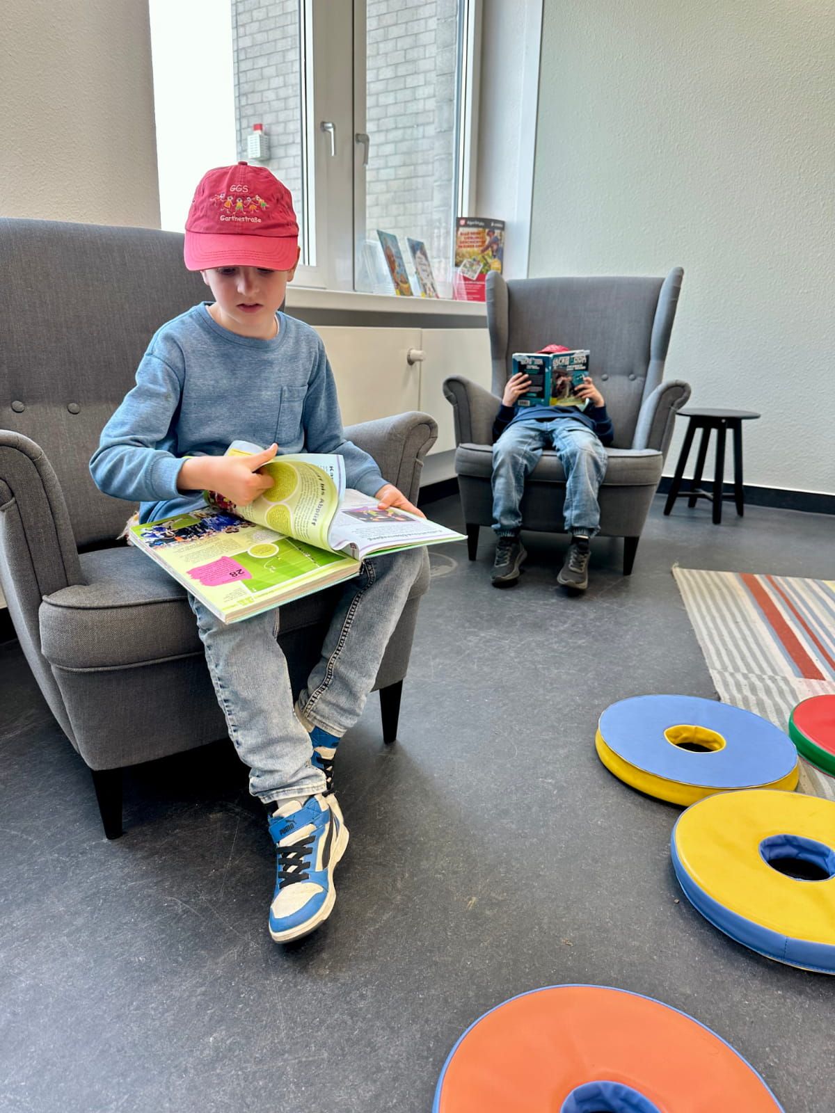 zwei Kinder lese ein Buch in Sesseln sitzend