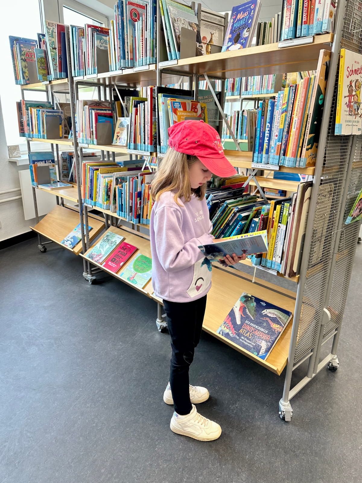 ein Kind liest ein Buch vor einem Bibliotheksregal