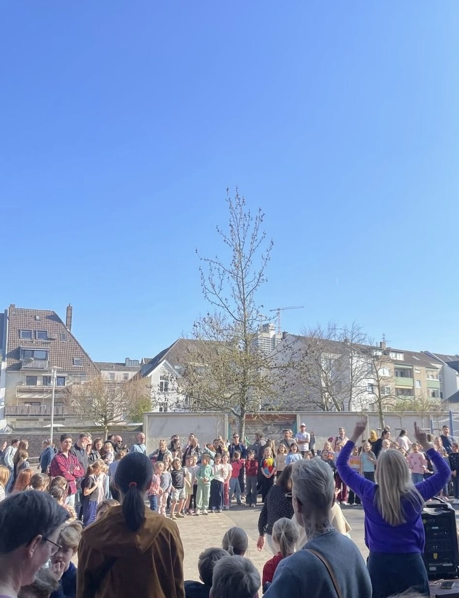 Schulkinder und Lehrpersonen sind auf dem Schulhof im Kreis versammelt