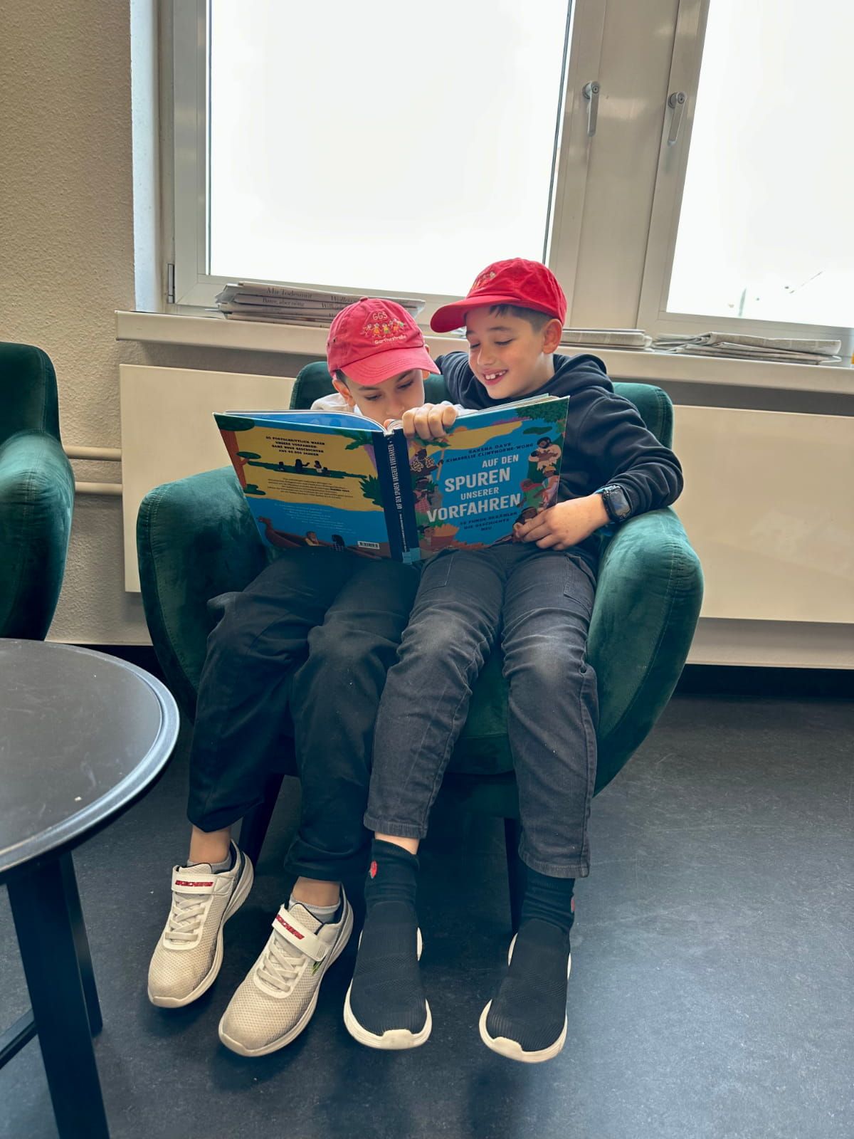 zwei Kinder sitzen auf einem Sessel und lesen ein Buch