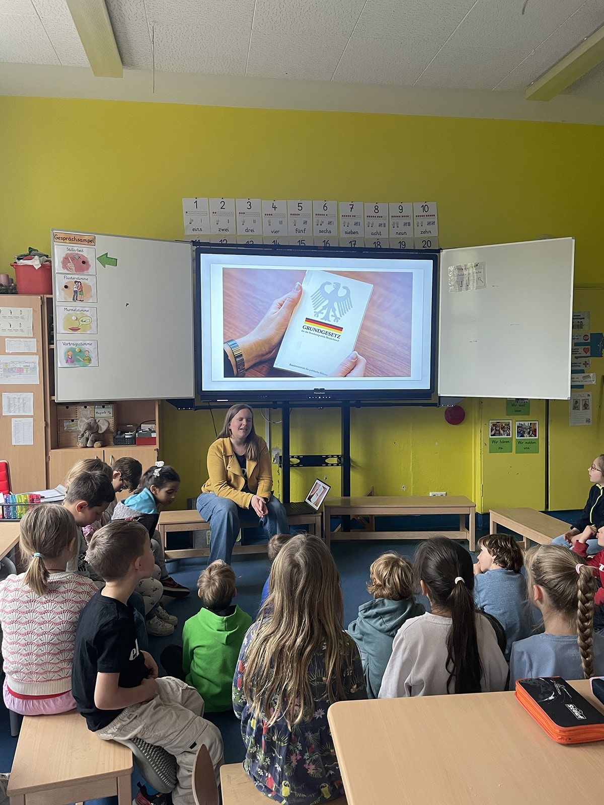 Kinder sitzen im Klassenraum im Kreis und hören einen Vortrag zum Thema Grundgesetz