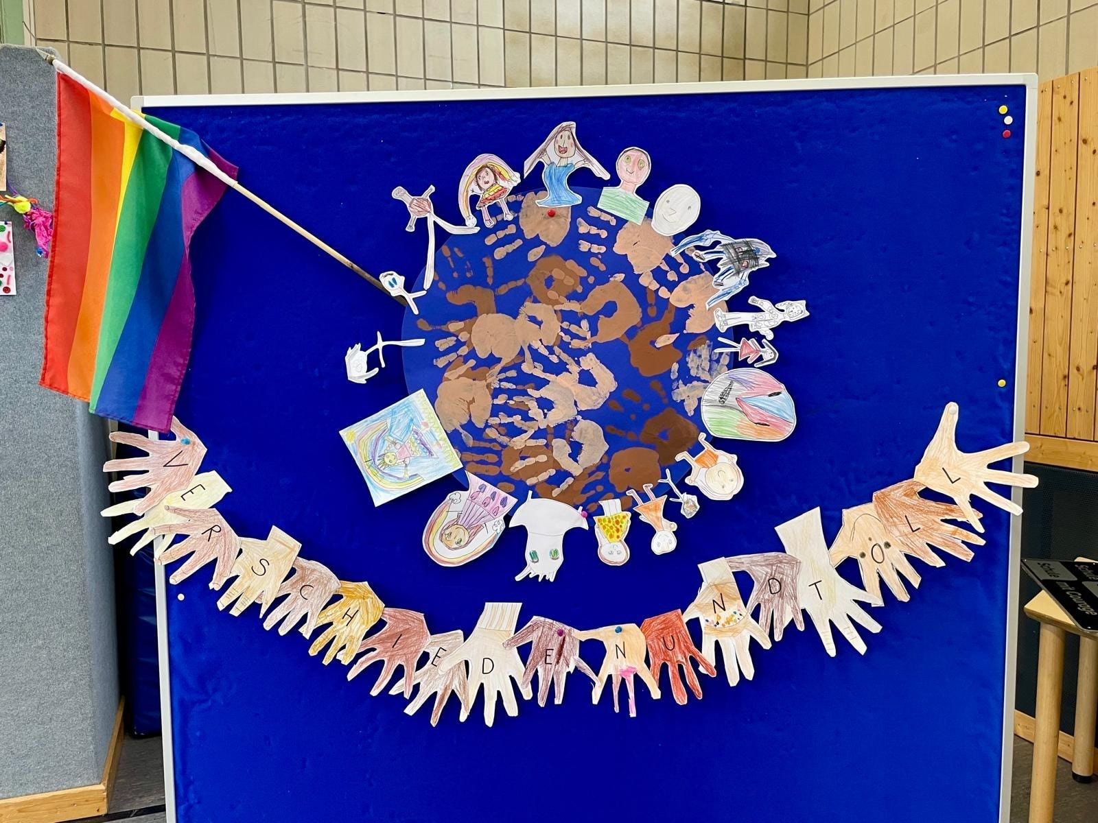 Tafel mit gezeichneten Bildern von vielfältigen Menschen, zusammen mit Händen und einer Pride-Flagge