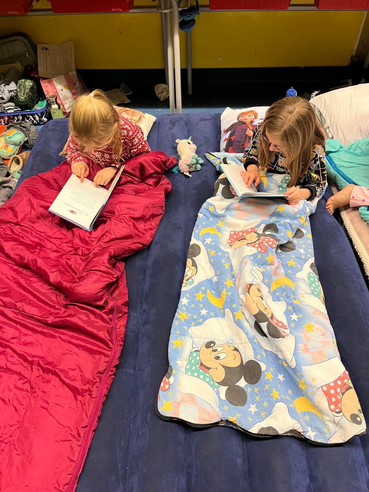 2 Kinder lesen in ihren Schlafsäcken auf einer Luftmatratze