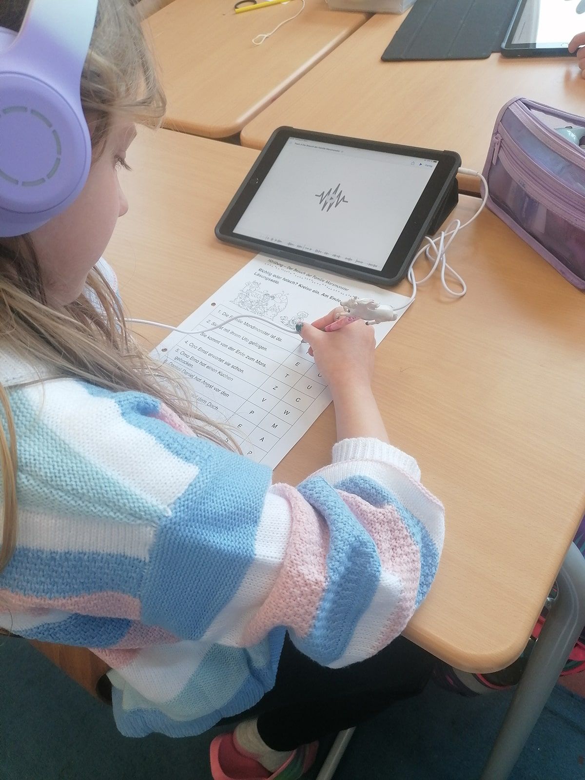 Kind hört eine Zuhörgeschichte auf einem Tablet und schreibt auf einem Arbeitsblatt