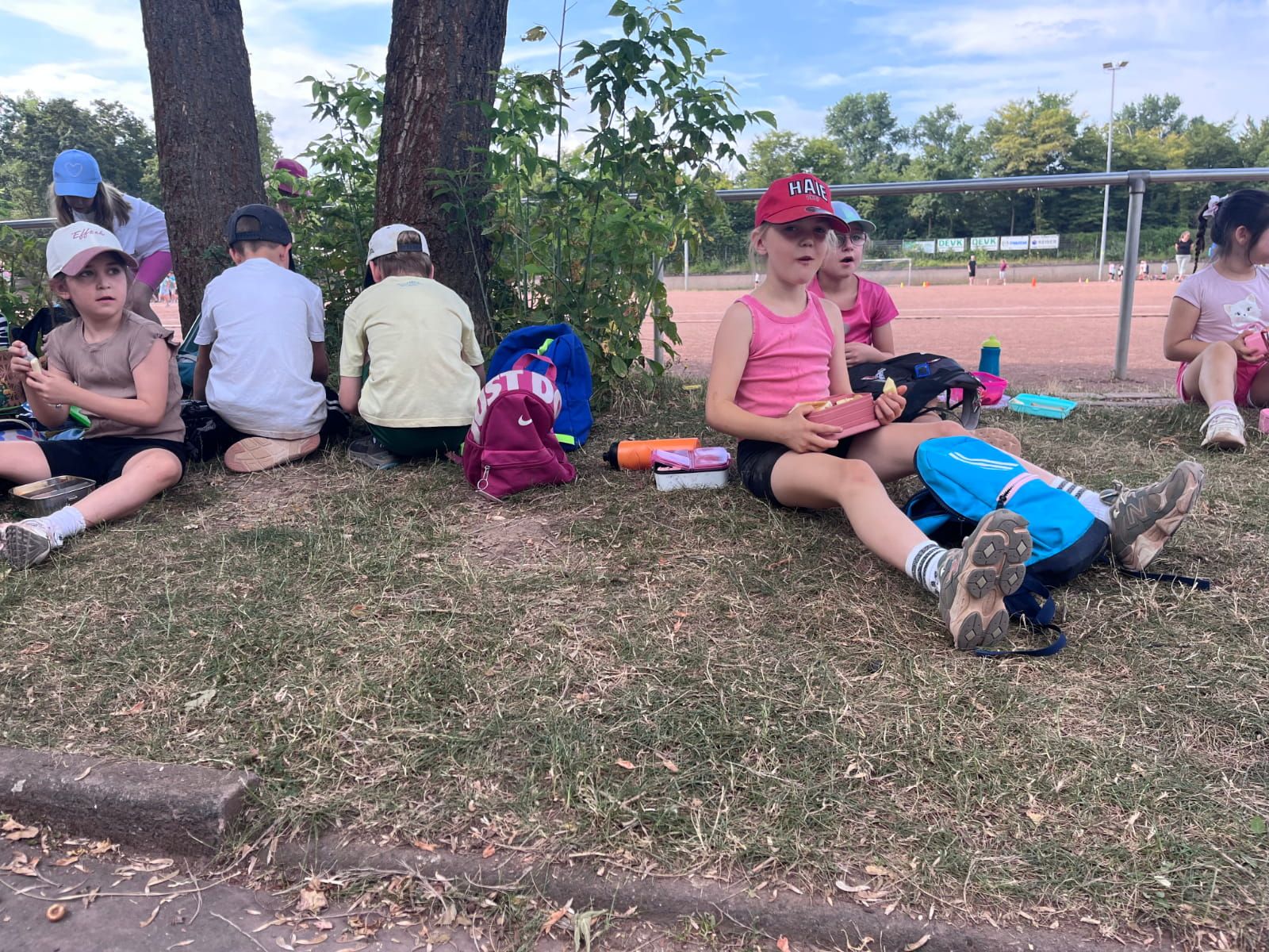 Kinder machen Pause am Sportplatz unter einem Baum