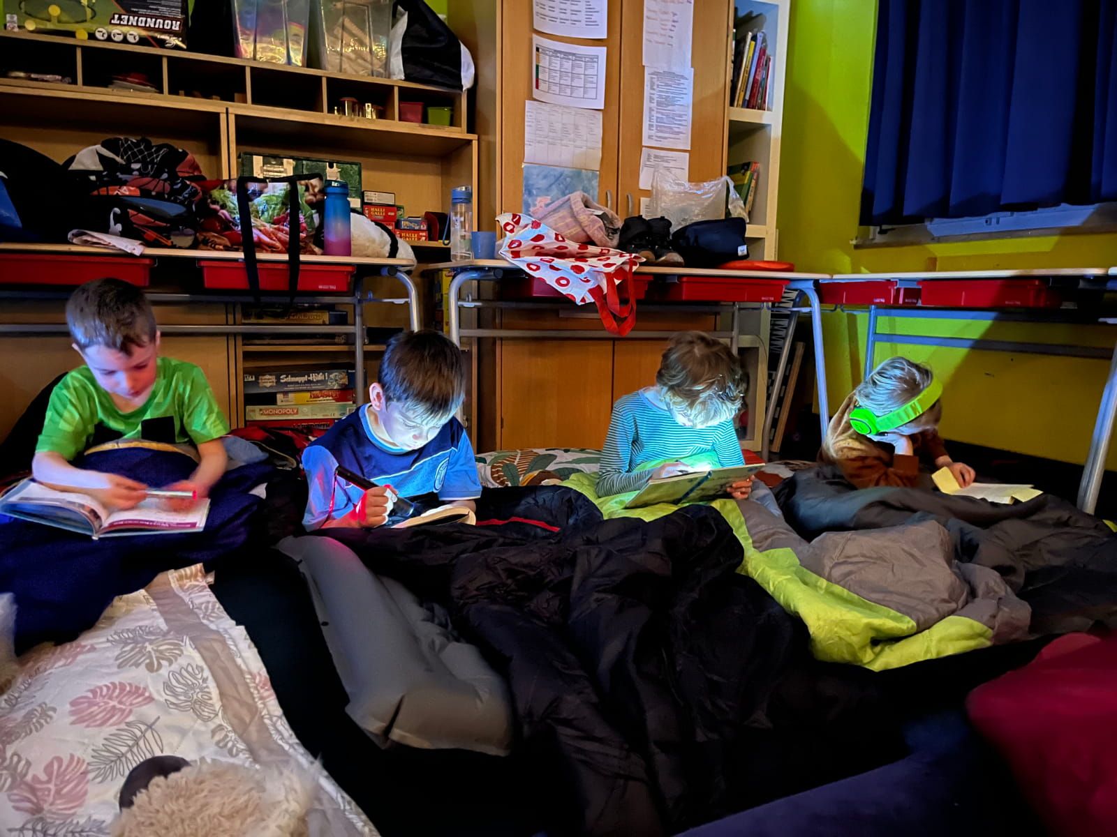 4 Kinder lesen zum Teil mit Taschenlampen in ihren Schlafsäcken