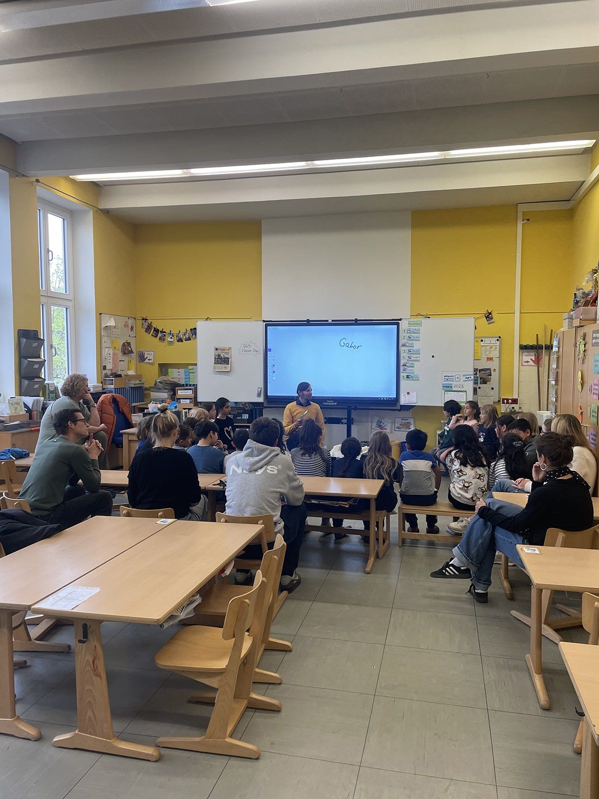 Kinder und Lehrpersonen sitzen im Kreis und hören einem Vortrag zu