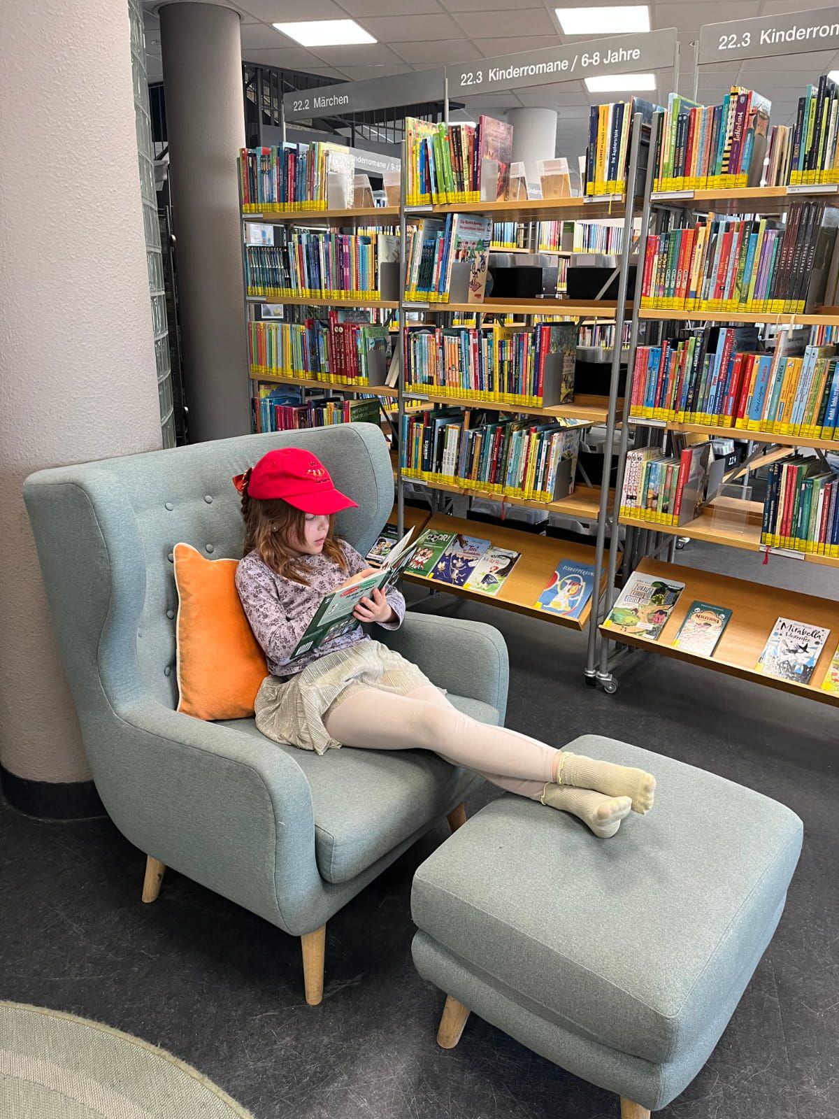 ein Kind liest ein Buch auf einem Sessel mit einem Hocker für die Füße