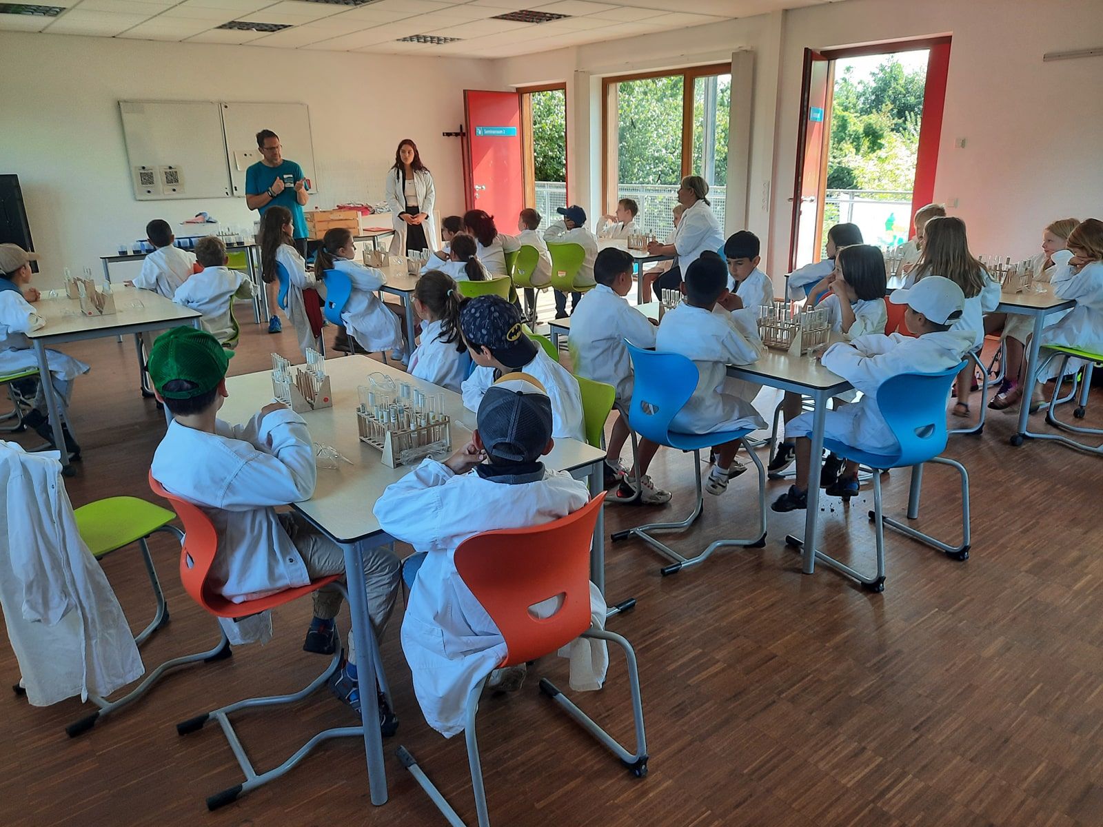 Kinder in Kitteln experimentieren an Tischen mit Reagenzgläsern